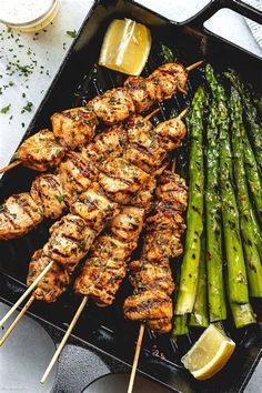 chicken and asparagus skewers on a grill with lemon wedges next to them