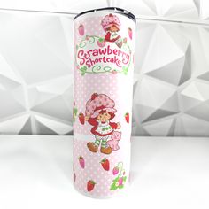 a pink and white cup with strawberry shortcakes on the side, in front of a geometric background