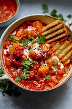 a bowl of tomato soup with grilled bread and parmesan cheese on the side