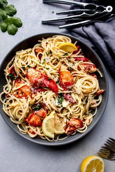 a bowl of pasta with lobster and lemons on the side next to a fork