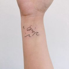 a small tattoo on the wrist of a person with a dolphin in the ocean and stars