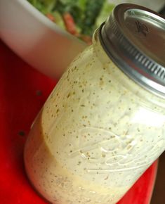 a mason jar filled with dressing sitting on top of a red cutting board next to a bowl of salad