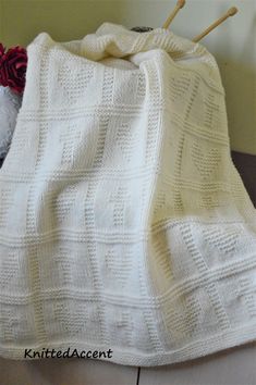 a white knitted blanket sitting on top of a wooden floor next to a stuffed animal