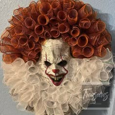 a creepy clown with red hair and orange curls on it's face is hanging from the wall