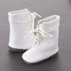 a pair of white baby shoes with laces on the top and bottom, sitting on a gray surface