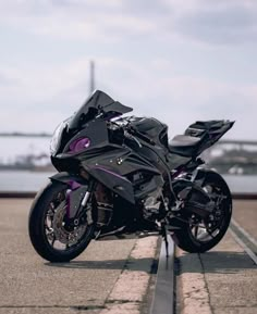 a black and purple motorcycle parked on the side of a road next to a body of water