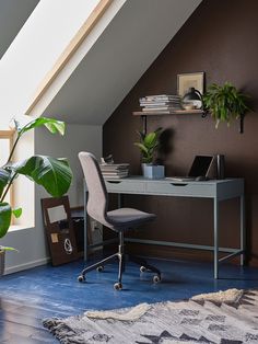 a desk with a laptop on top of it in a room next to a potted plant