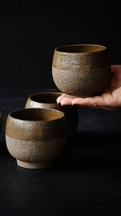 a person holding three bowls in their hand on a black surface with another bowl behind them