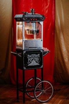 an old fashioned popcorn machine sitting on top of a wooden floor next to a red curtain