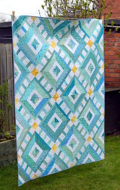 a blue and yellow quilt hanging from a clothes line in the grass next to a brick building