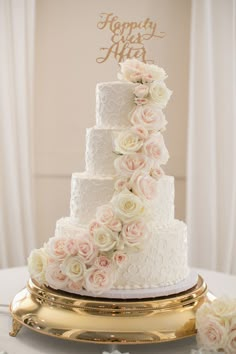 a white wedding cake with pink flowers on top and gold lettering that says happily after