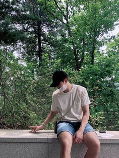 a young man sitting on top of a cement wall wearing a baseball cap and shorts