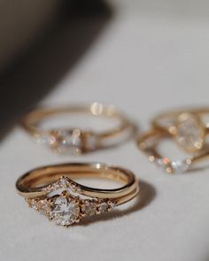 three gold wedding rings sitting on top of a white table next to two diamond engagement rings