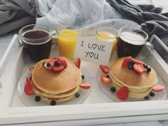 two pancakes with strawberries and blueberries are on a tray next to glasses of orange juice