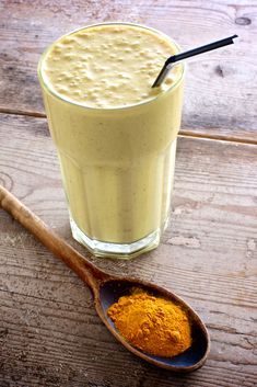 a wooden spoon with some food in it next to a glass filled with orange liquid