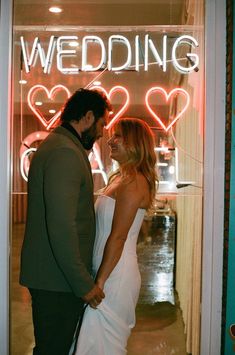 a man and woman are standing in front of a neon sign that says wedding on it