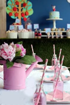 a pink watering can filled with flowers and drinking straws on a table set for a tea party