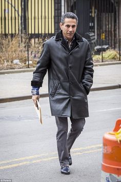 a man walking down the street with an umbrella in his hand and wearing a coat