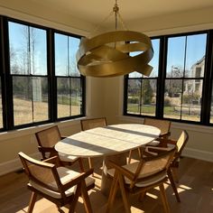 a dining room table with chairs and a large window in the back ground, looking out onto an open field