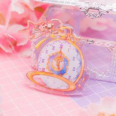 a small clock keychain sitting on top of a pink table next to flowers