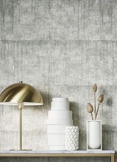 two white vases and a gold lamp on a shelf in front of a concrete wall