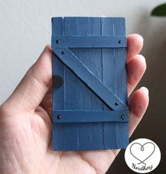 a hand holding a miniature blue piece of wood in it's left hand with the door open