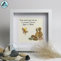 a white frame with some rocks and flowers on it, next to a small plant