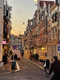 people walking and riding bicycles on a city street with christmas lights strung across the buildings