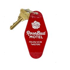 a red bottle shaped keychain with a rose bud motel logo on it