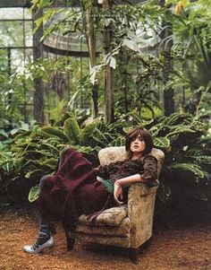 a woman laying on top of a chair next to a forest filled with green plants