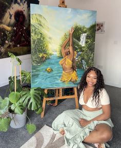 a woman sitting on the floor in front of an easel with paintings behind her