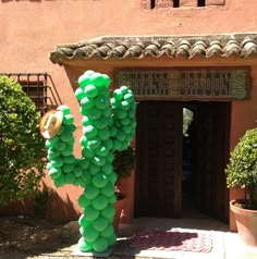 a large cactus made out of balloons in front of a building with potted plants