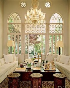 a living room filled with furniture and a chandelier hanging from the ceiling next to two large windows