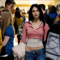 a woman in jeans and a pink shirt is walking through an airport with other people