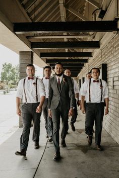 a group of men in suits and ties walking down a sidewalk next to a brick wall