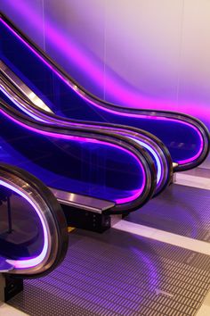 an escalator with purple and blue lights on the wall next to each other