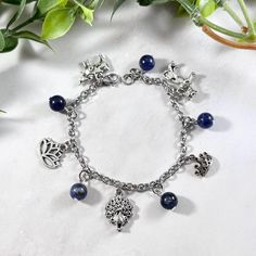 a silver bracelet with charms and blue beads on top of a white table next to green leaves