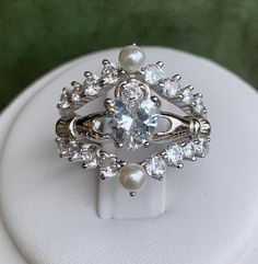 a close up of a ring on top of a white stand with pearls and diamonds