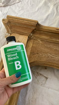 a person holding a bottle of wood b in front of a wooden frame with the letter b painted on it