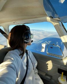 a woman sitting in the cockpit of an airplane with headphones on and looking out