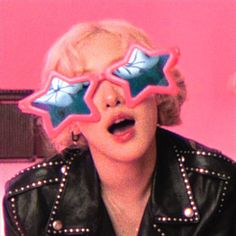 a woman in black jacket and pink glasses with stars on their eyes looking at the camera