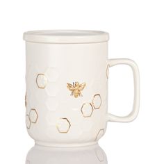 a white ceramic mug with gold honeycombs on the side and a bee in the middle