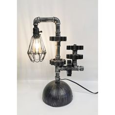 a lamp made out of pipes and wires on top of a metal base with a light bulb attached to it