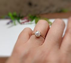 a woman's hand holding a ring with a white pearl on the middle of it