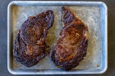 two pieces of meat sitting on top of a metal baking pan next to each other