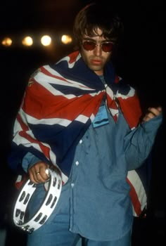 a man in an union jack jacket holding a white frisbee and wearing sunglasses