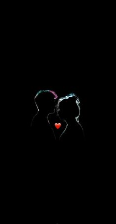 two people standing in the dark with their faces close to each other and one is holding a red heart