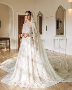 a woman in a white wedding dress standing on a wooden floor with her veil pulled back