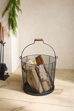 a wire basket with logs in it sitting on the floor next to a candle holder