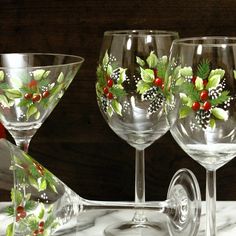 three wine glasses with holly and berries painted on the glass are sitting on a marble table